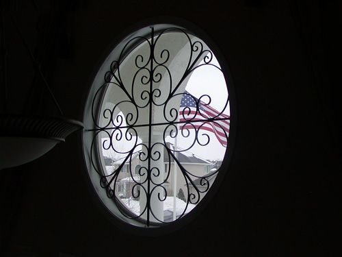 A round window with a wrought iron fence and an american flag behind it.