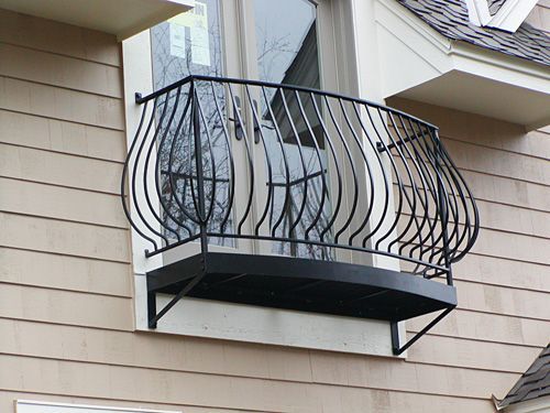 A balcony on the side of a house with a wrought iron railing