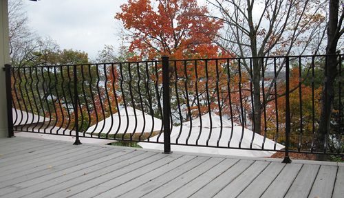 A deck with a wrought iron railing overlooking a lake.