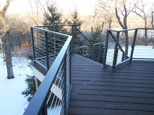 A wooden deck with a metal railing and trees in the background