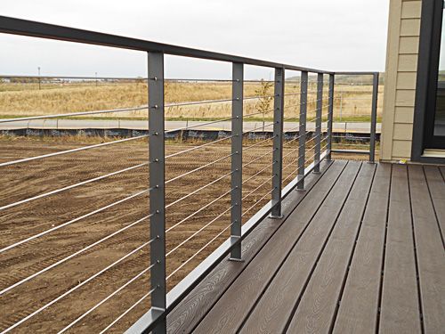 A wooden deck with a metal railing and a field in the background.
