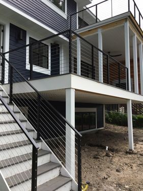 A house with stairs leading up to a deck with a black railing.