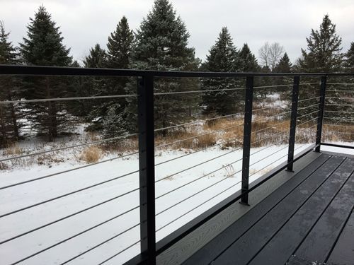 A balcony with a stainless steel railing overlooking a snowy forest.