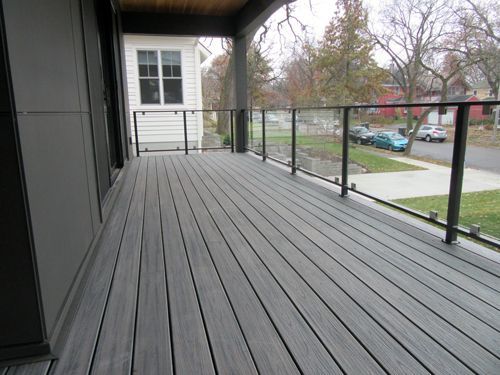 A gray deck with a glass railing and a white house in the background