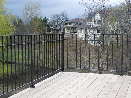 A wooden deck with a metal railing and a house in the background.