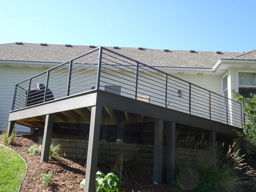 A wooden deck with a metal railing is in front of a house.