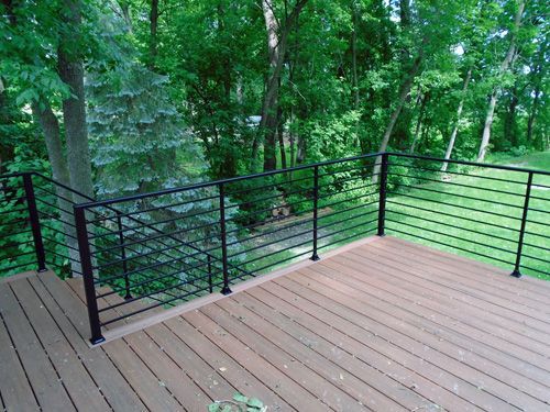 A wooden deck with a black railing and trees in the background.
