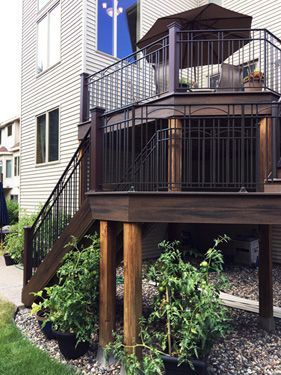 A wooden deck with a metal railing and stairs next to a house.