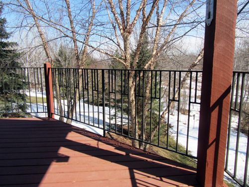 A wooden deck with a metal railing overlooking a snowy forest.