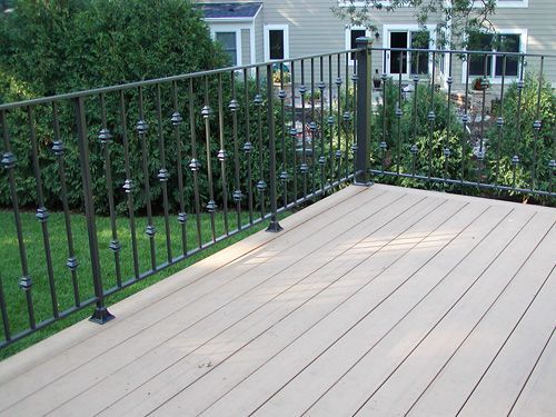 A deck with a wrought iron railing and a house in the background