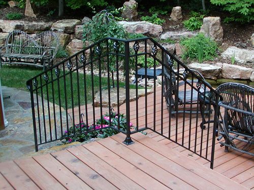 A wooden deck with a wrought iron railing and chairs