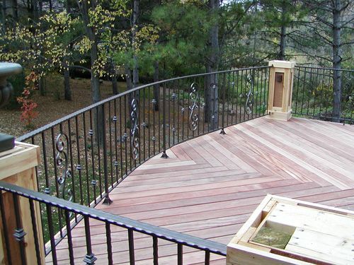 A wooden deck with a wrought iron railing surrounded by trees