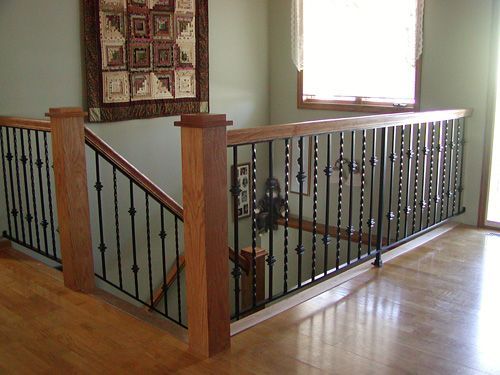 A wooden staircase with a wrought iron railing and a quilt on the wall.