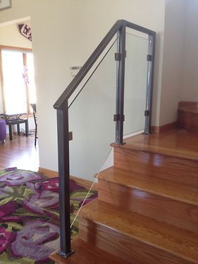 A wooden staircase with a glass railing and a rug on the floor.