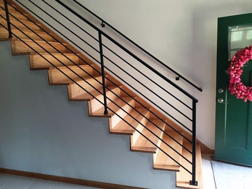 A wooden staircase with a black railing in front of a green door
