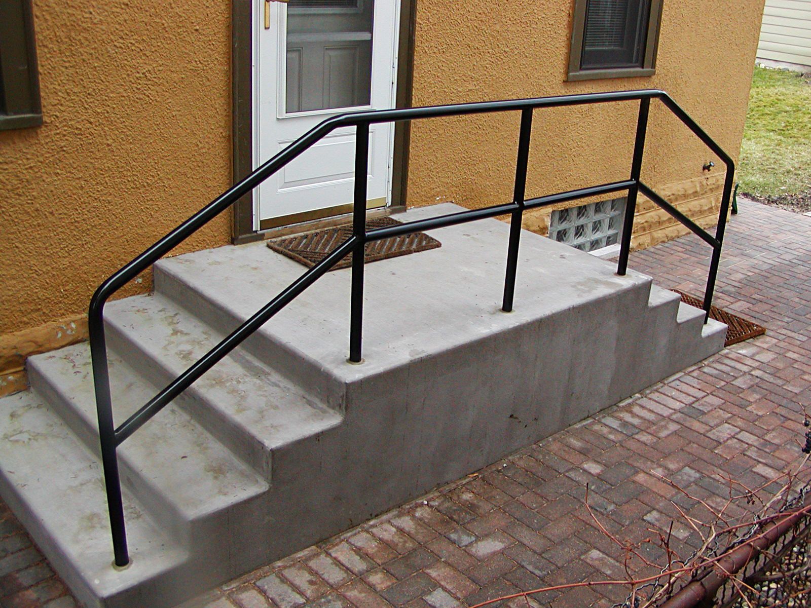Black metal handrails on concrete steps leading to a front door.
