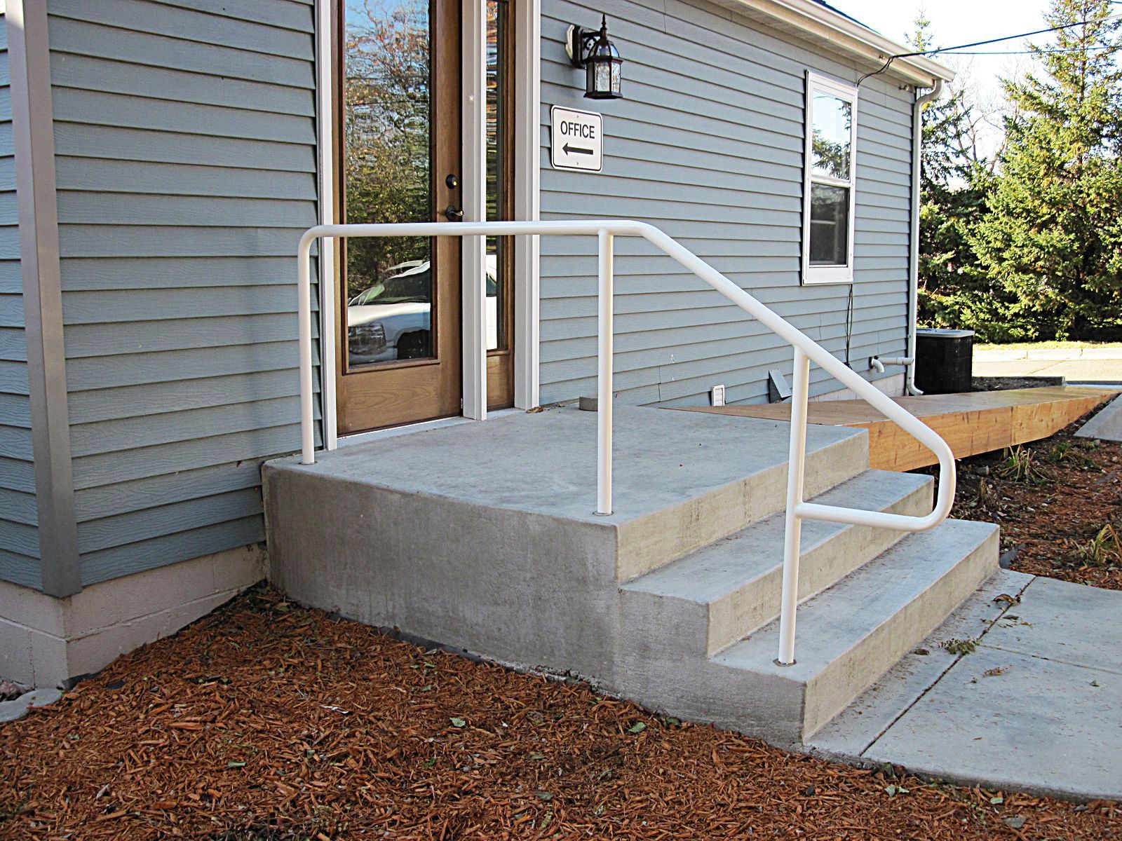Concrete steps with white handrail leading to a house entrance. Blue siding and door are visible.