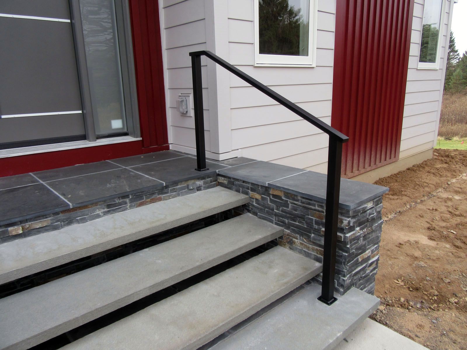 Black metal handrail on stone steps leading up to a house entrance.