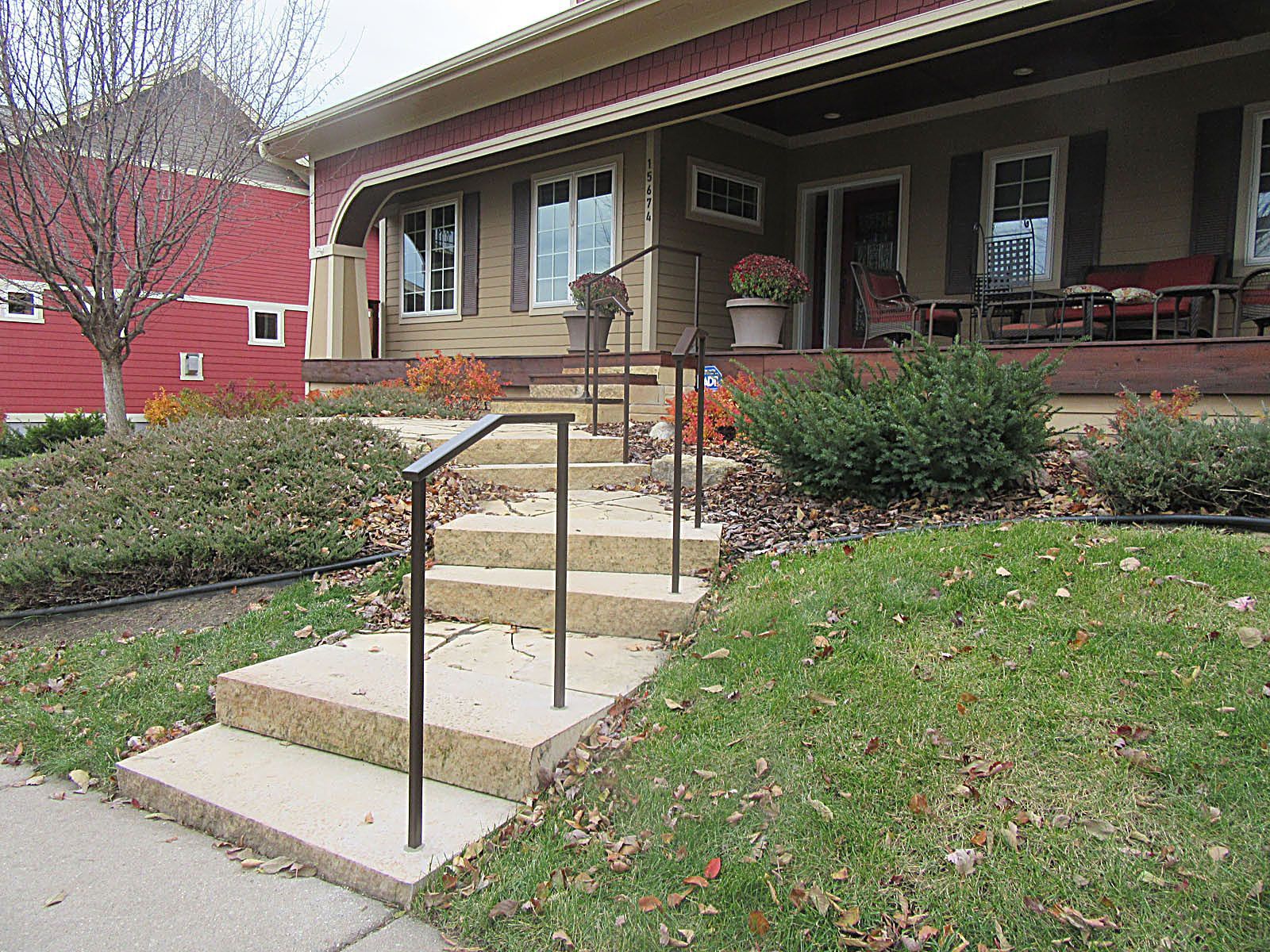 Concrete steps with handrails lead to a house with a porch; lawn and shrubs in front.