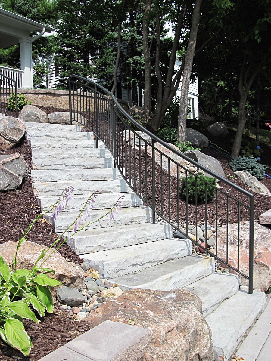 Stone steps with metal handrail ascend a landscaped hillside.