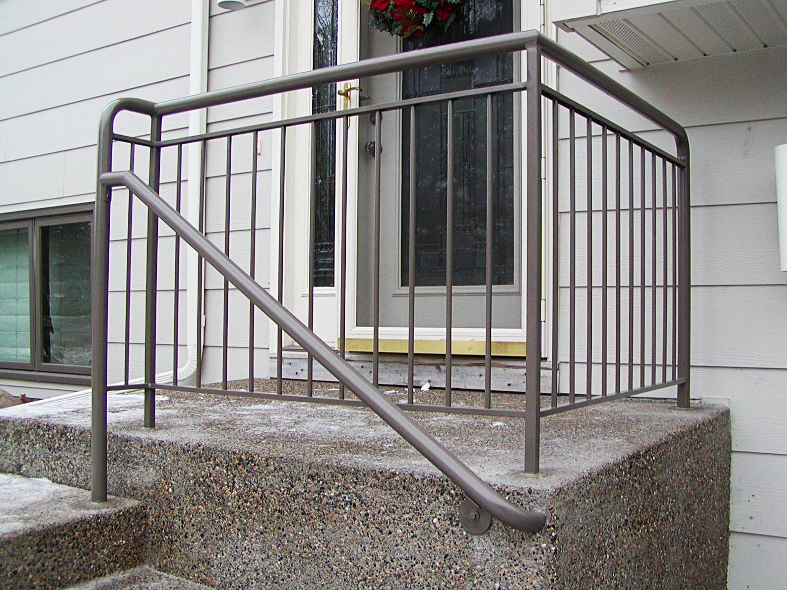 Gray metal railing on a concrete porch with steps leading to a front door.