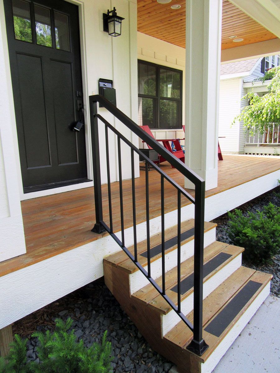 Black metal handrail on outdoor wooden steps leading to a white porch with a black door.