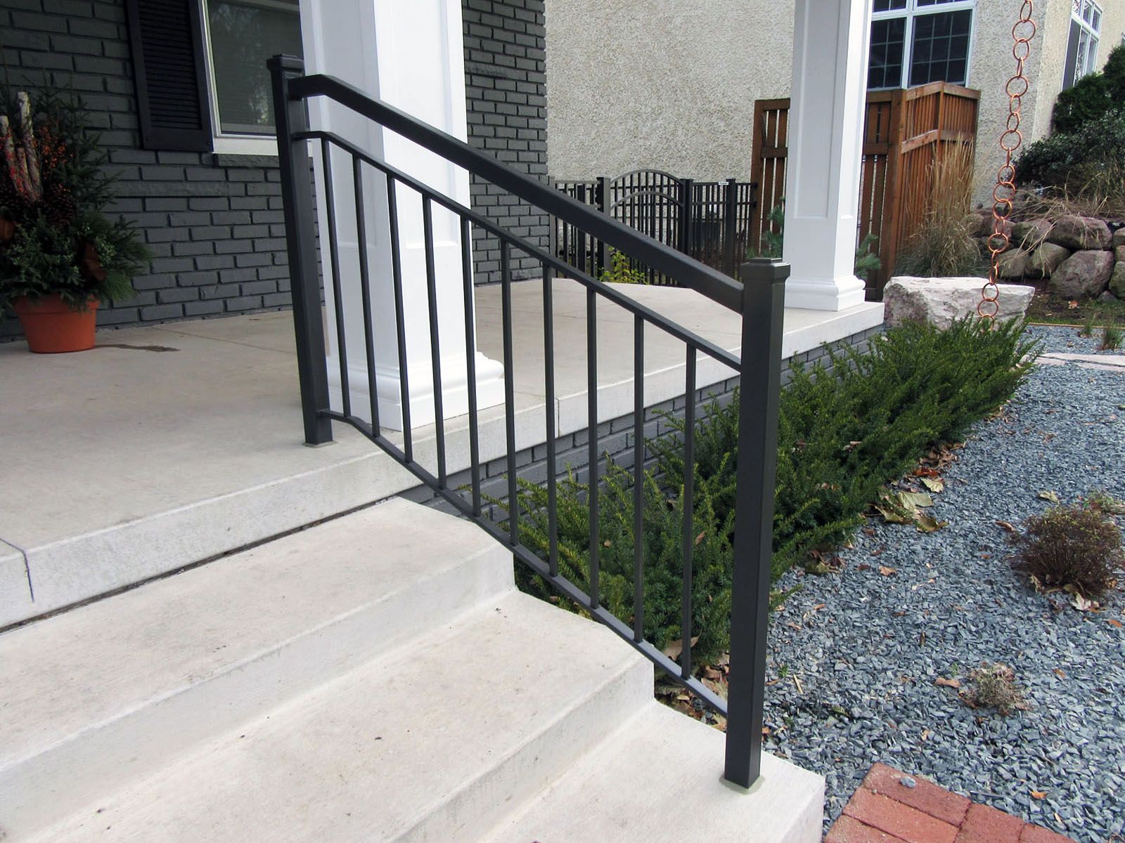 Black metal handrail on concrete steps leading to a porch with landscaping.