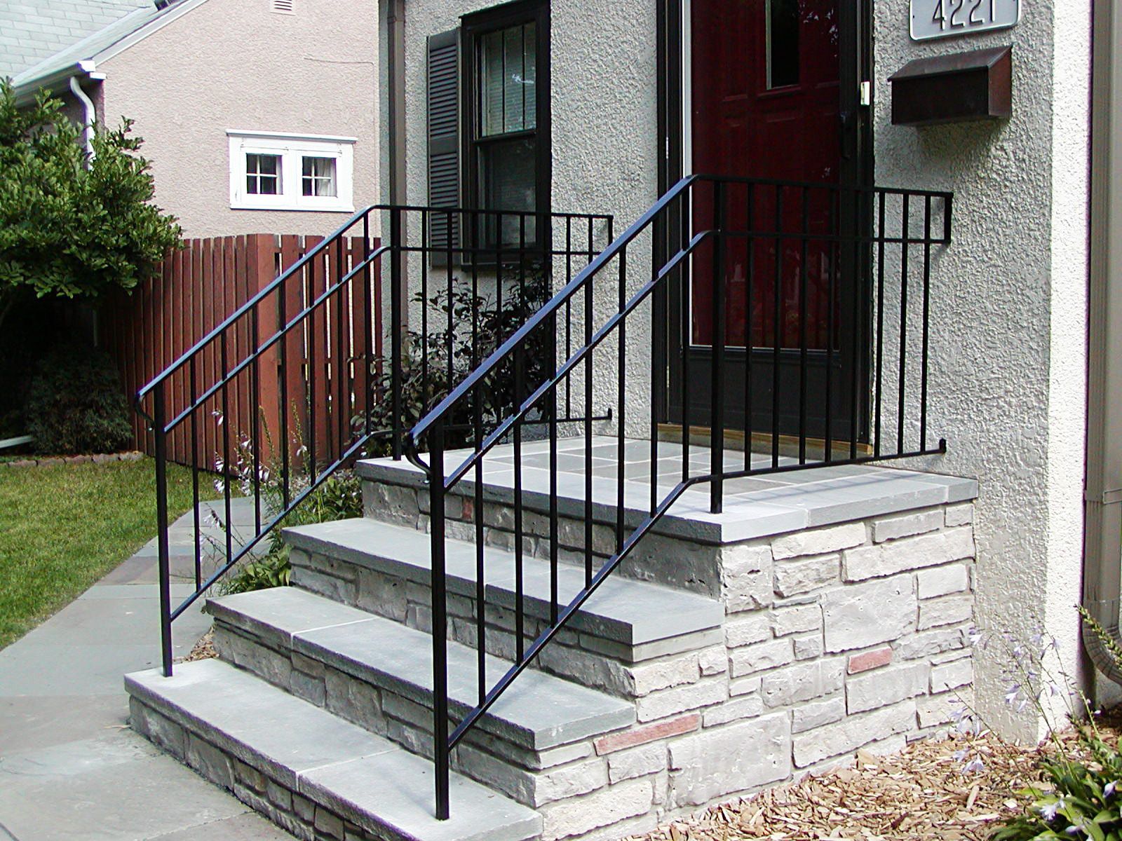 Black metal handrails on gray stone steps leading to a front door with a mailbox on the right.