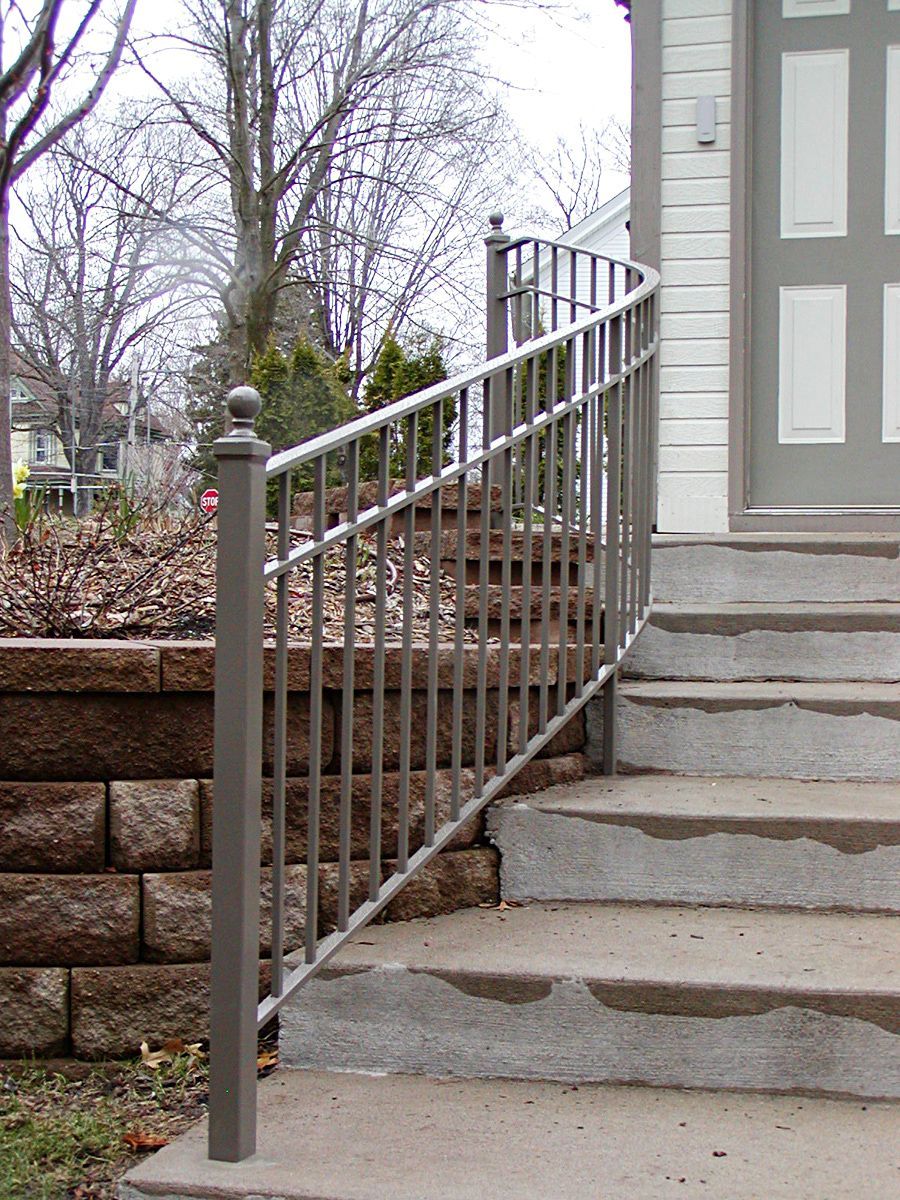 Metal railing curves down concrete steps next to a brick retaining wall.