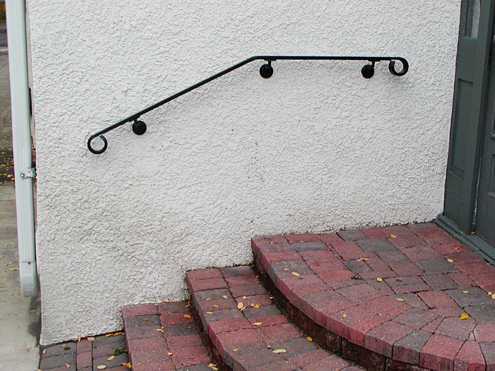 Black handrail on textured white wall above brick steps.