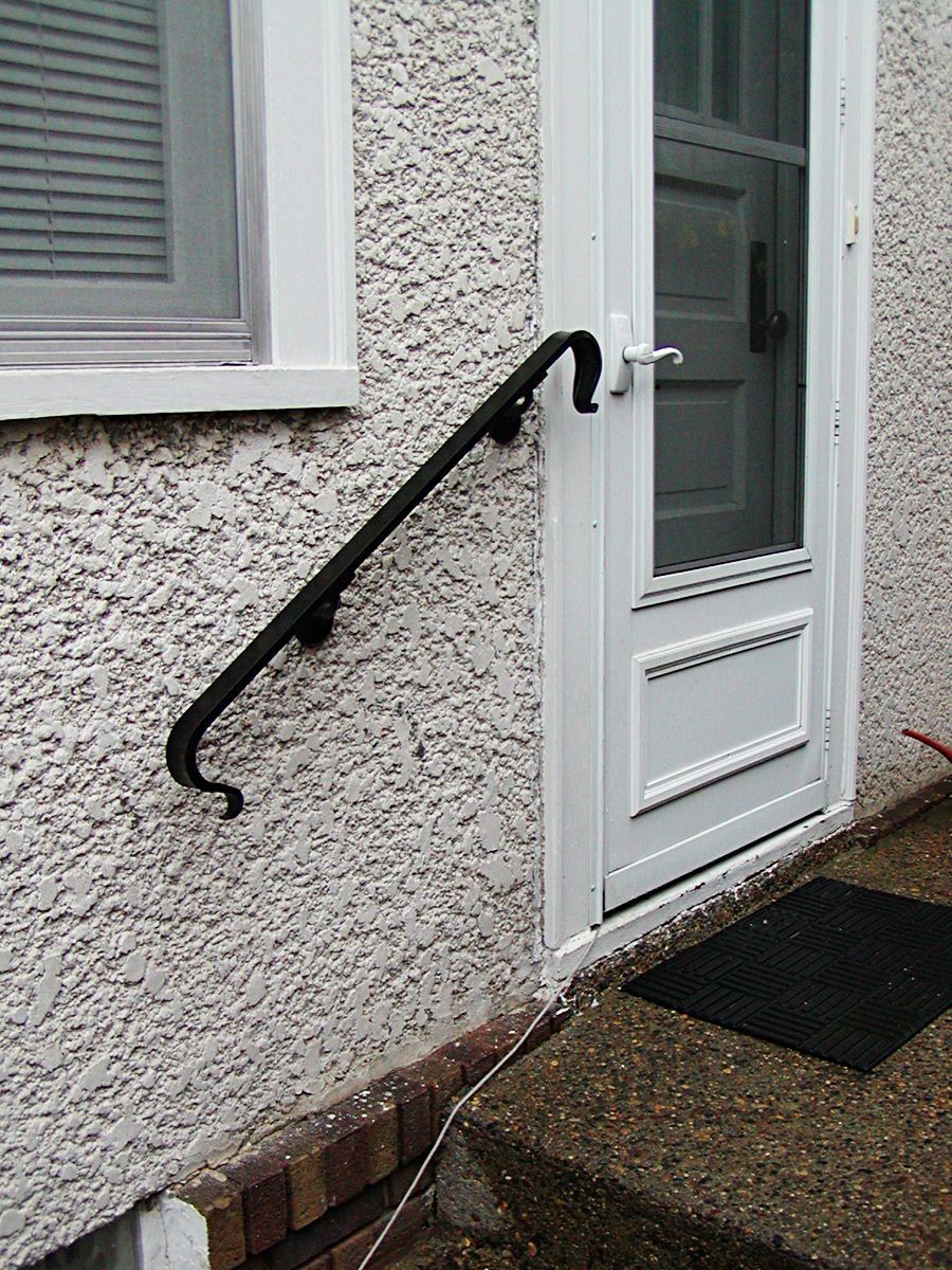 Black handrail mounted on a white textured wall next to a white door.
