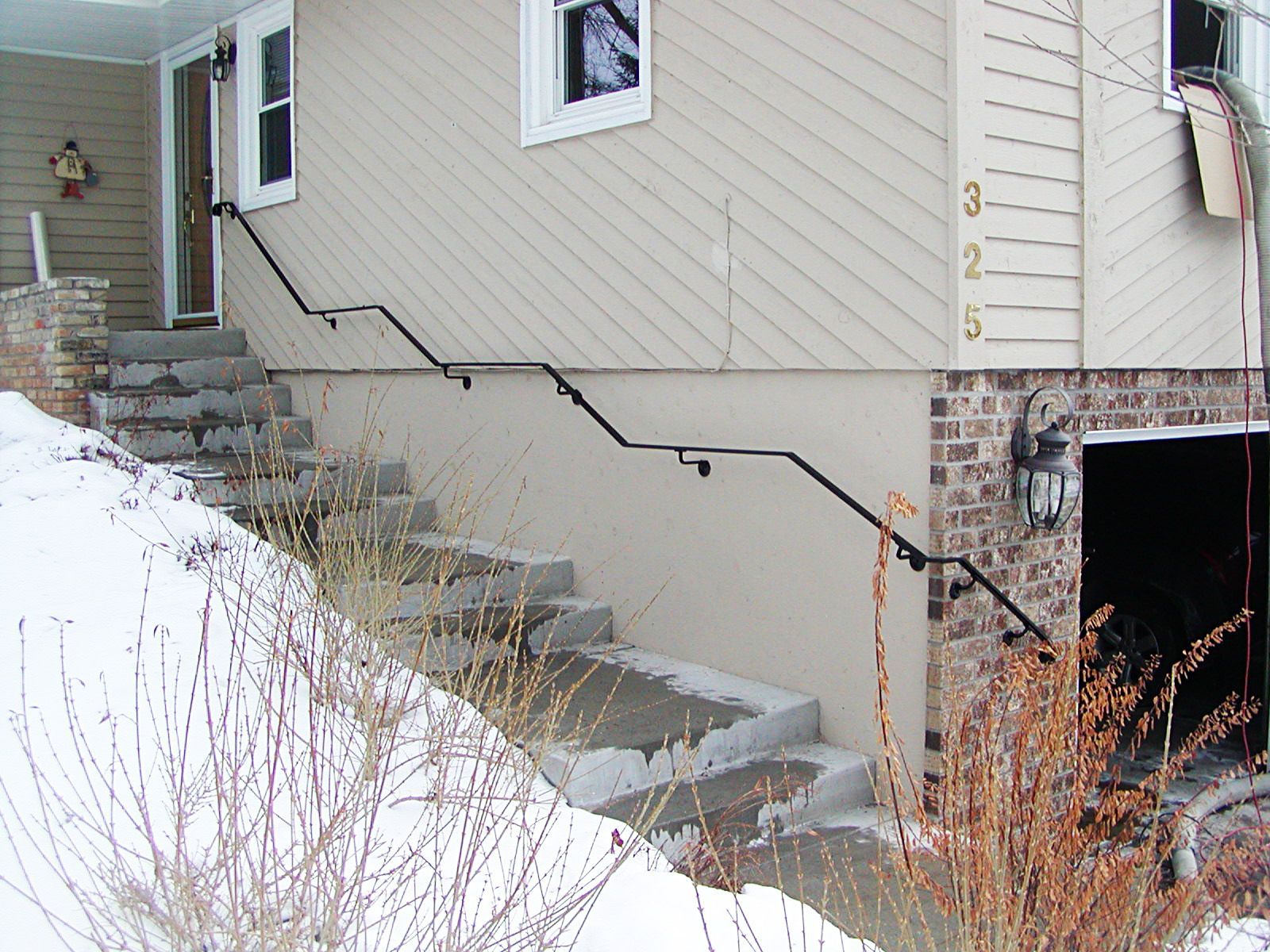 Exterior of a house with concrete steps, black handrails, and snow on the ground.