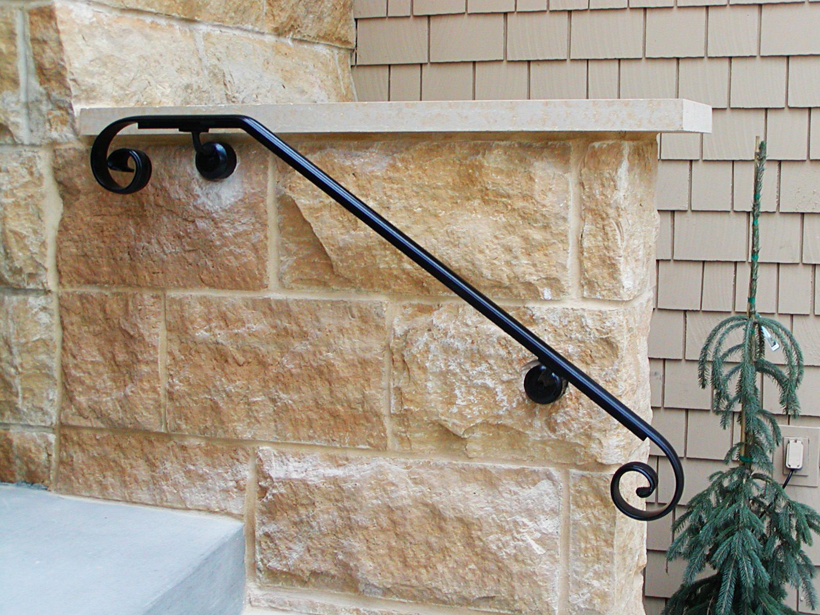 Black wrought iron handrail mounted on a stone wall, for accessibility.