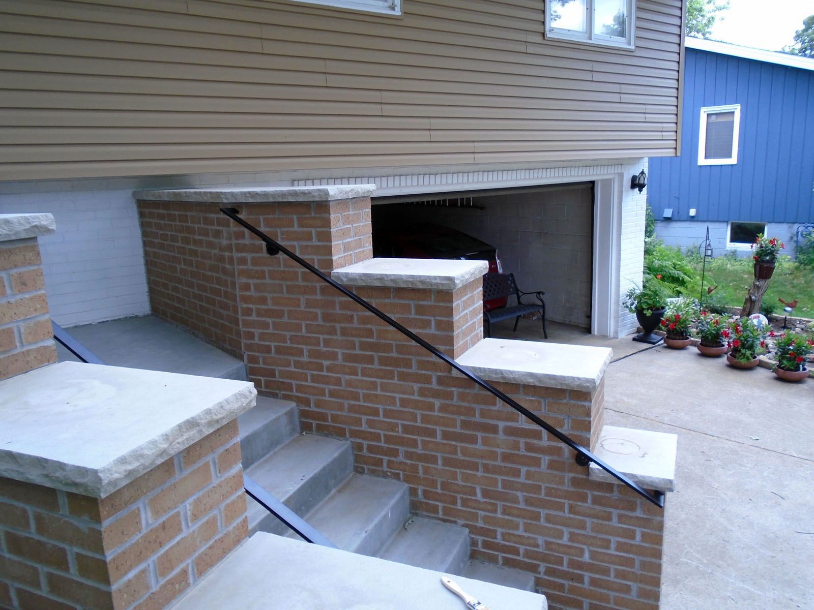 Brick steps leading to a house with a garage. A black handrail is present.
