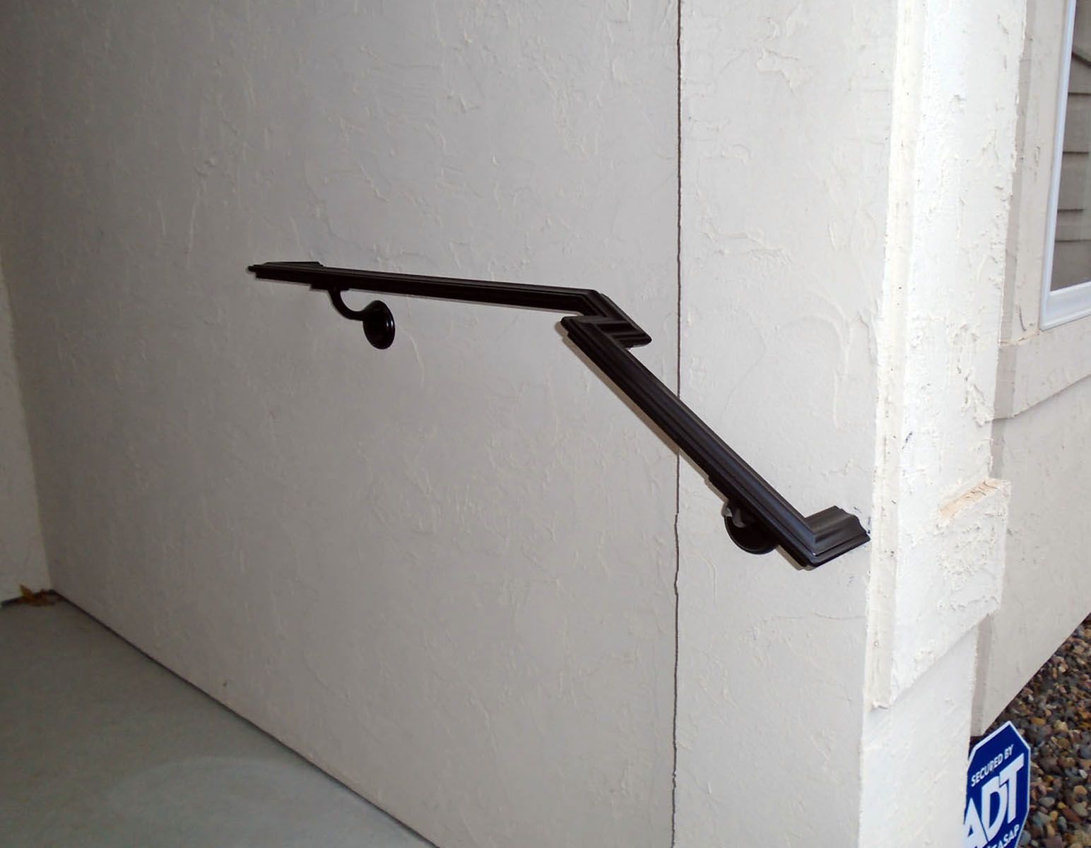 Black metal handrail on a white stucco wall outside a building.