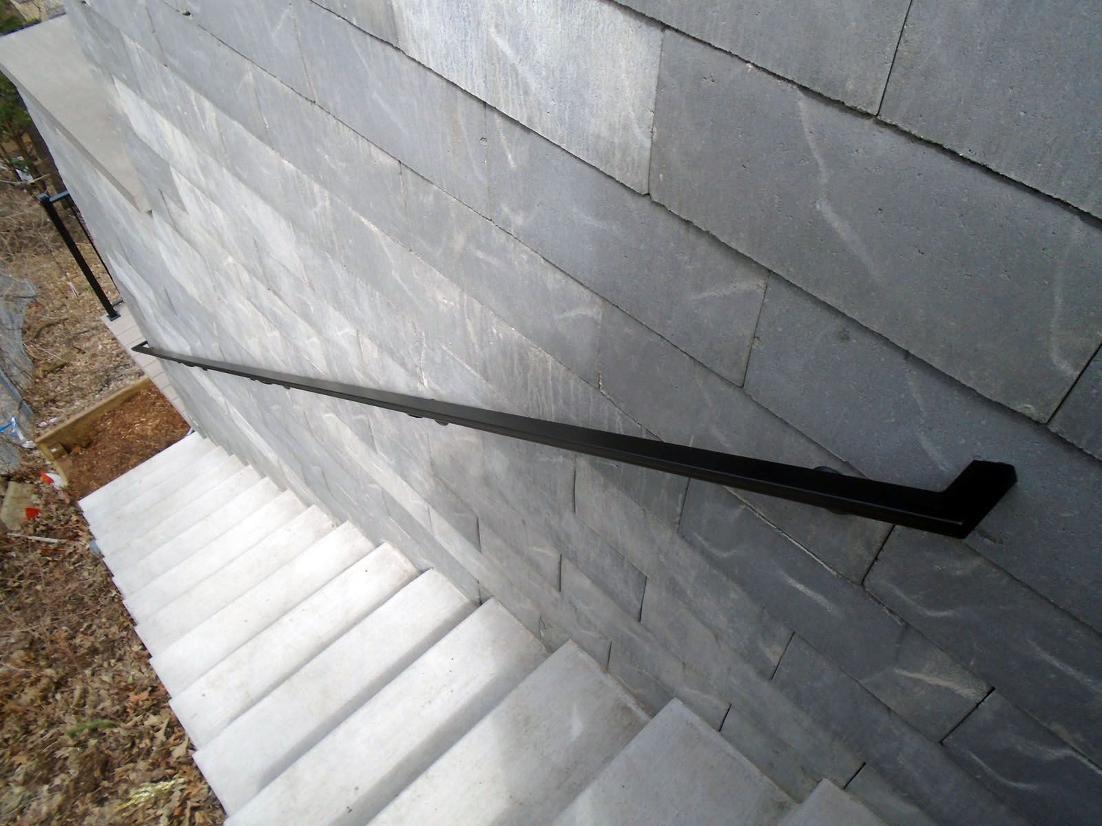 Staircase with gray stone wall and black metal handrail.