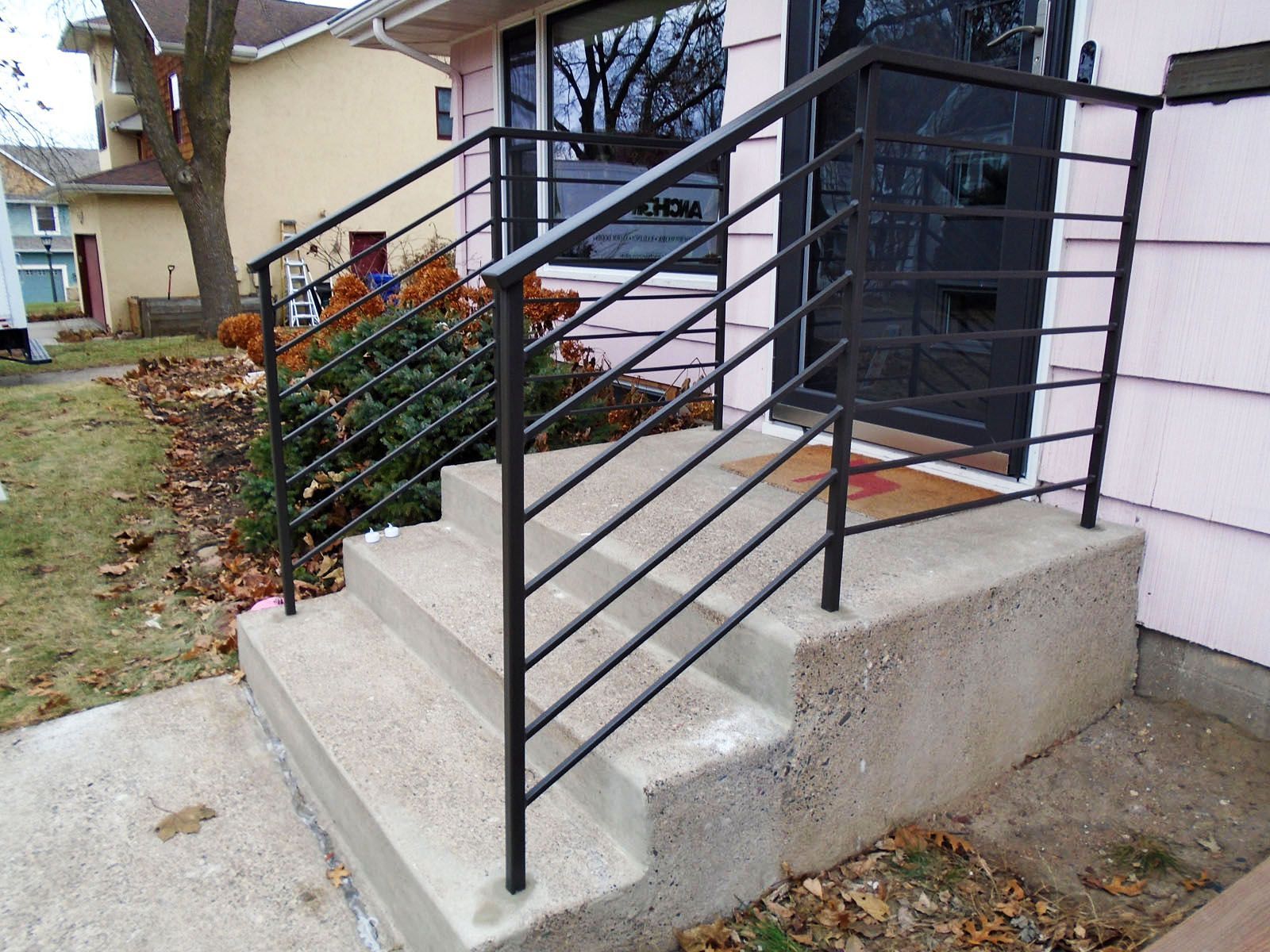 Concrete steps with black metal handrails leading to a front door of a light pink house.