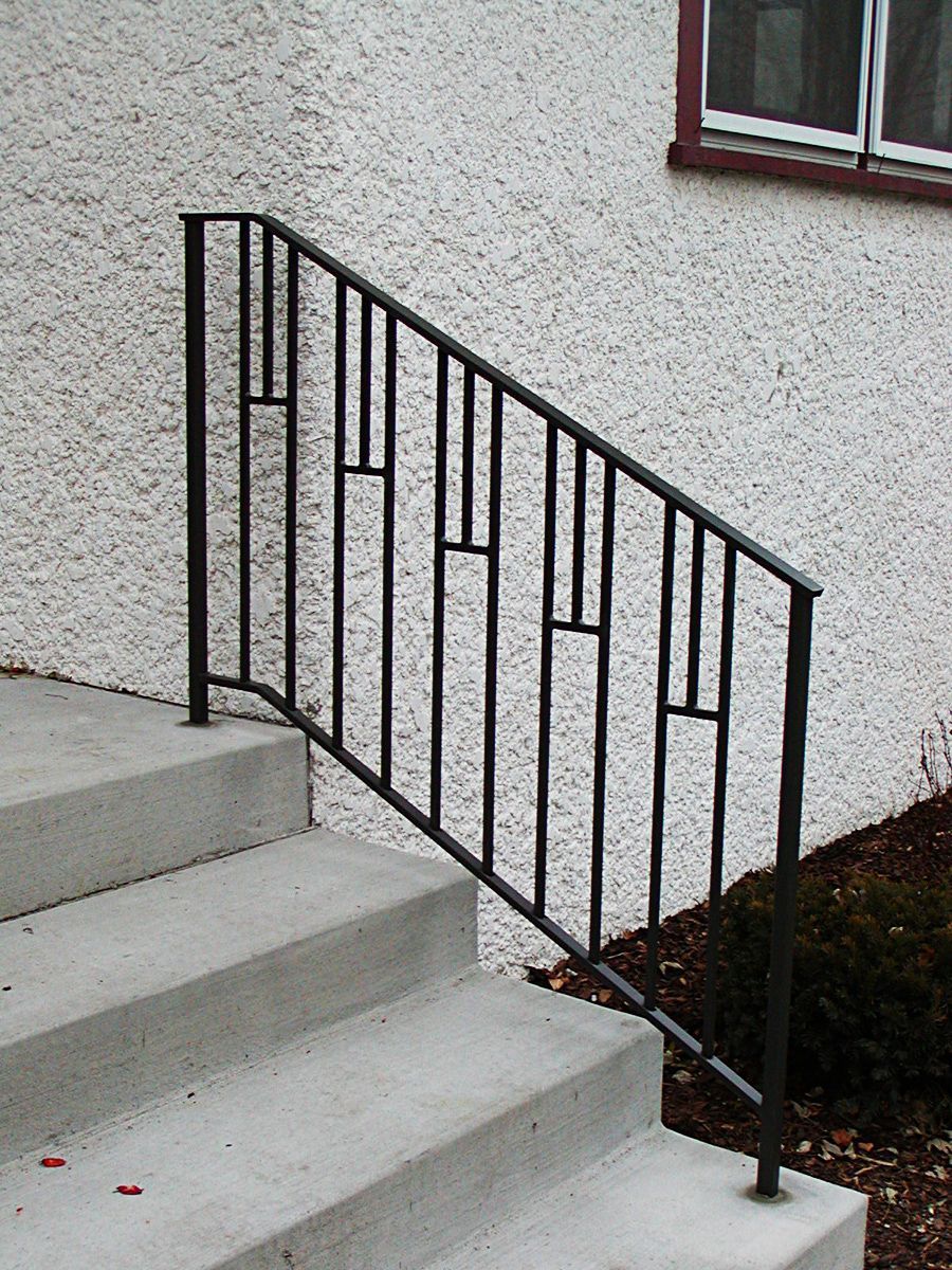 Black metal handrail on concrete steps, next to a textured white wall.