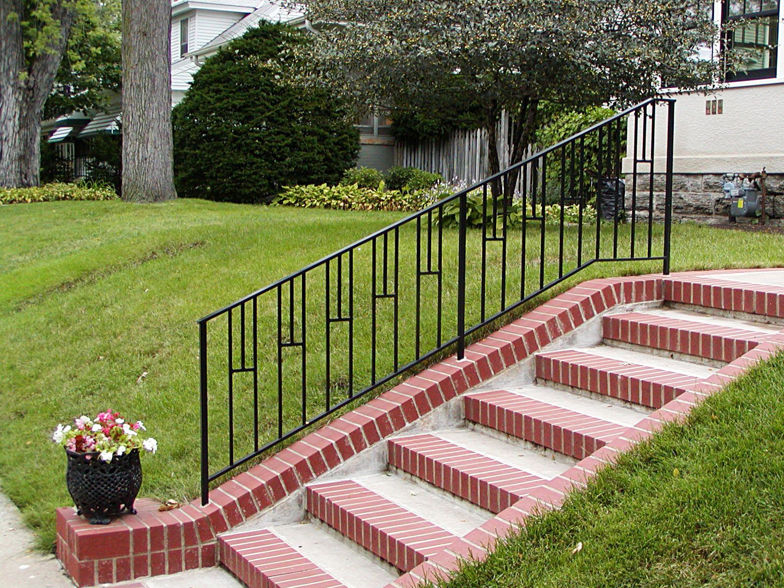 Brick steps with black metal railing on a grassy lawn leading to a house.