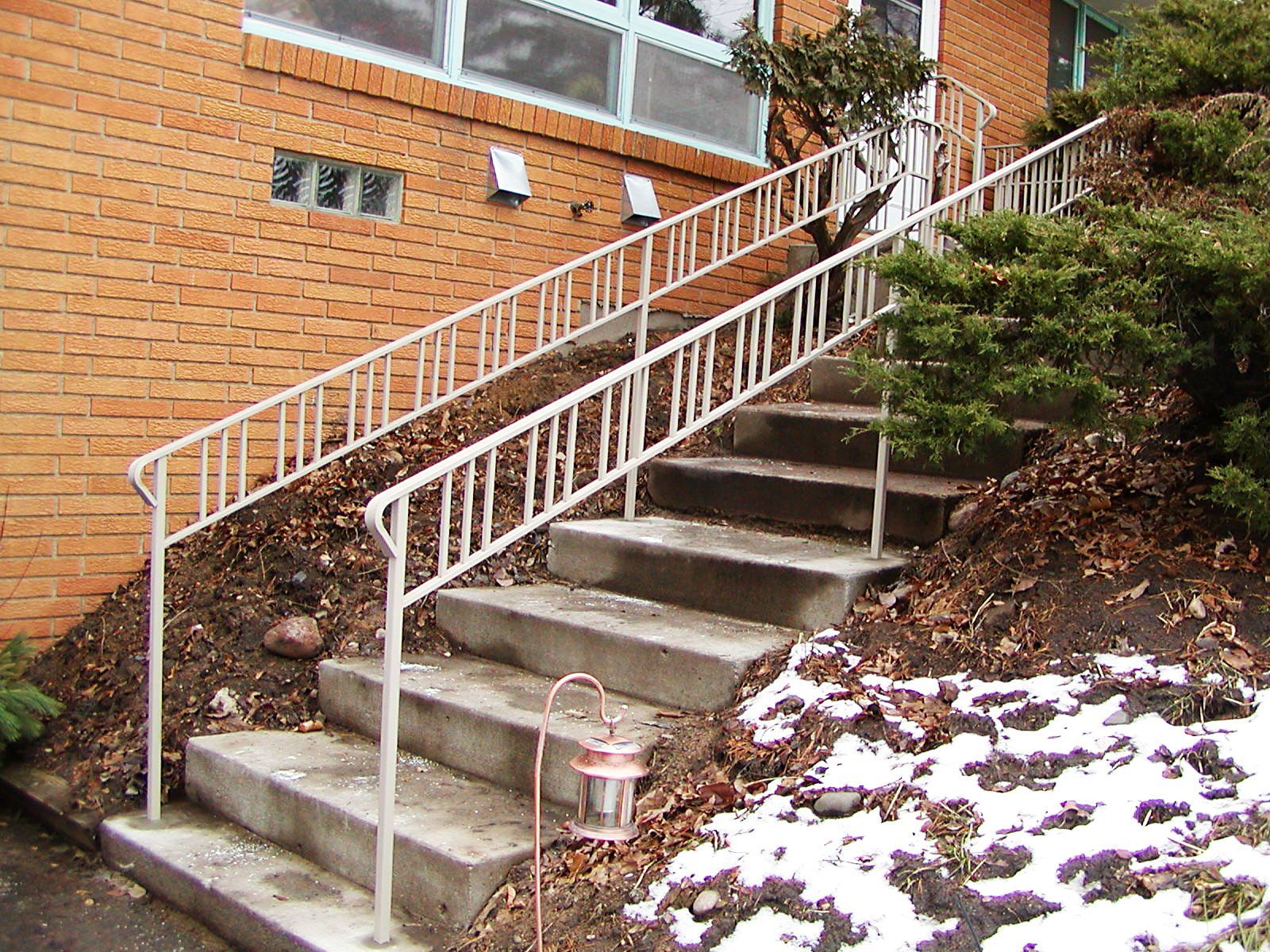 Concrete staircase with white metal handrails, leading to a brick building entrance.