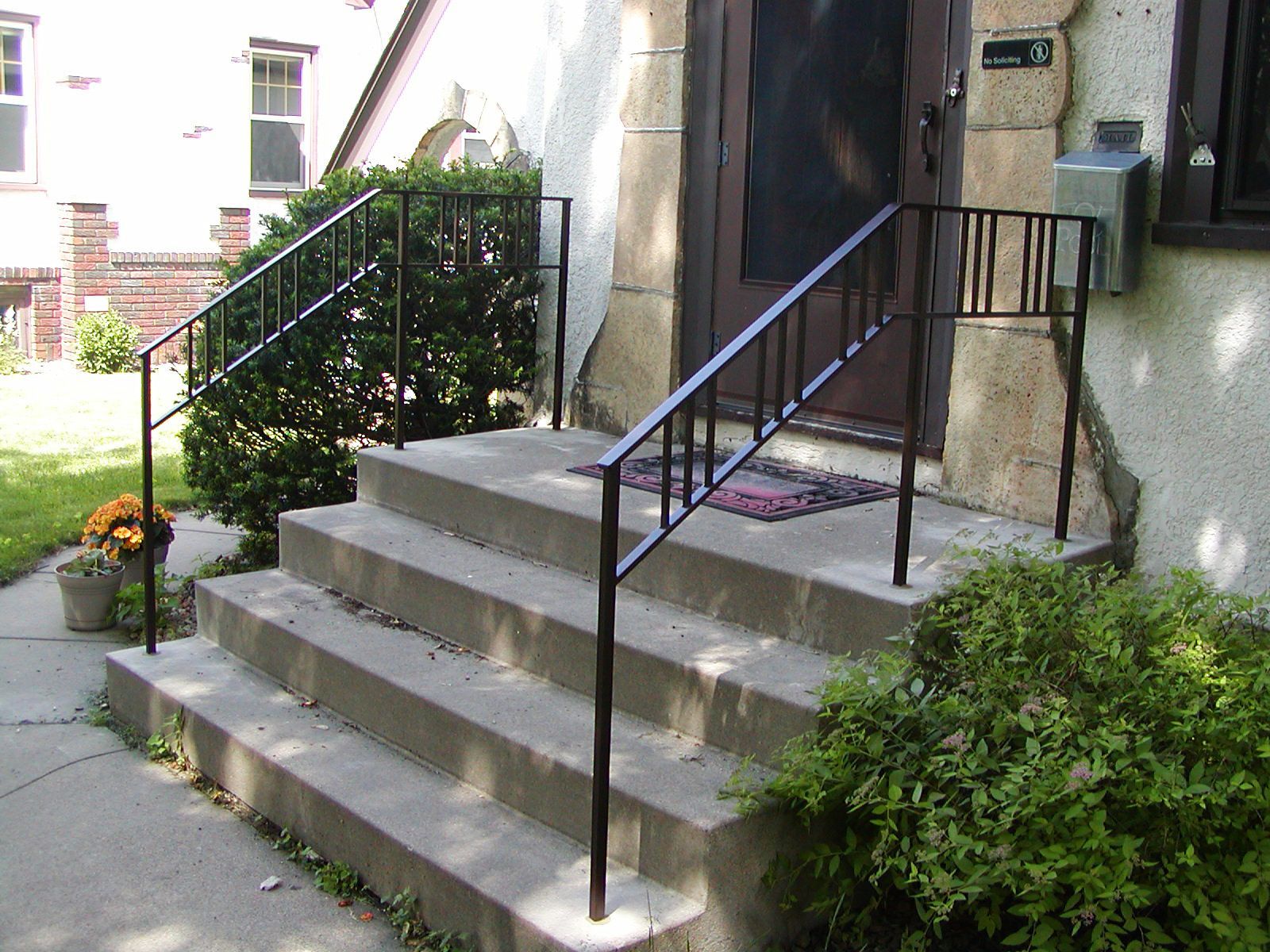 Concrete steps leading to a house entrance, black metal handrails.