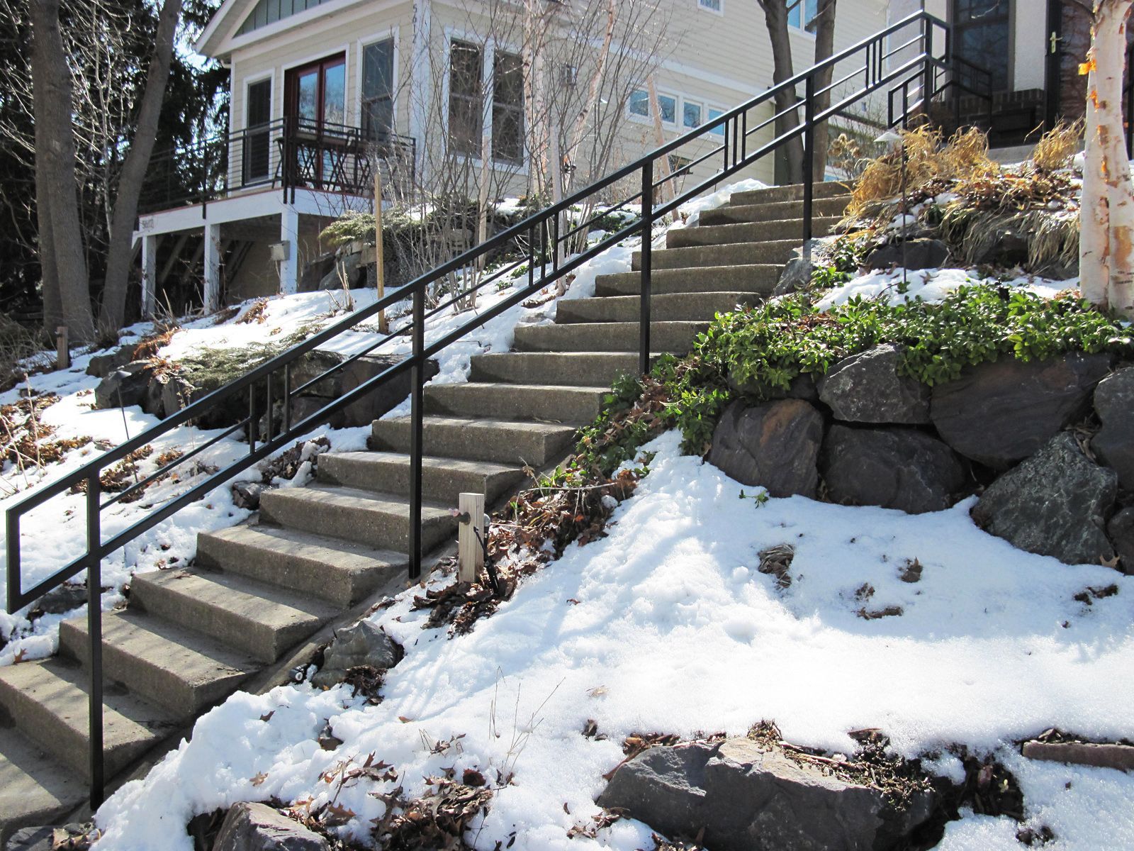 Staircase with black railing leading up to a house; snow on ground.