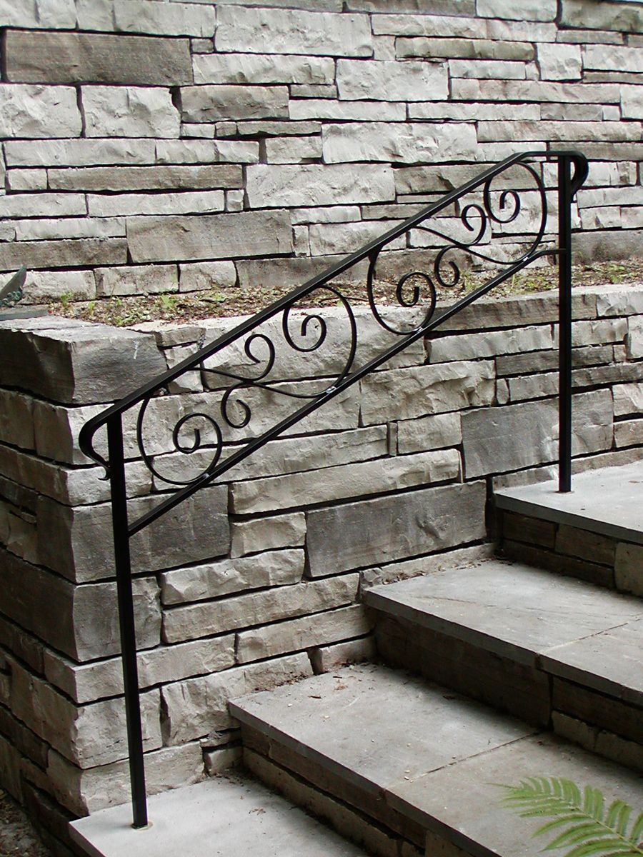Black wrought iron handrail on stone steps against a stacked stone wall.