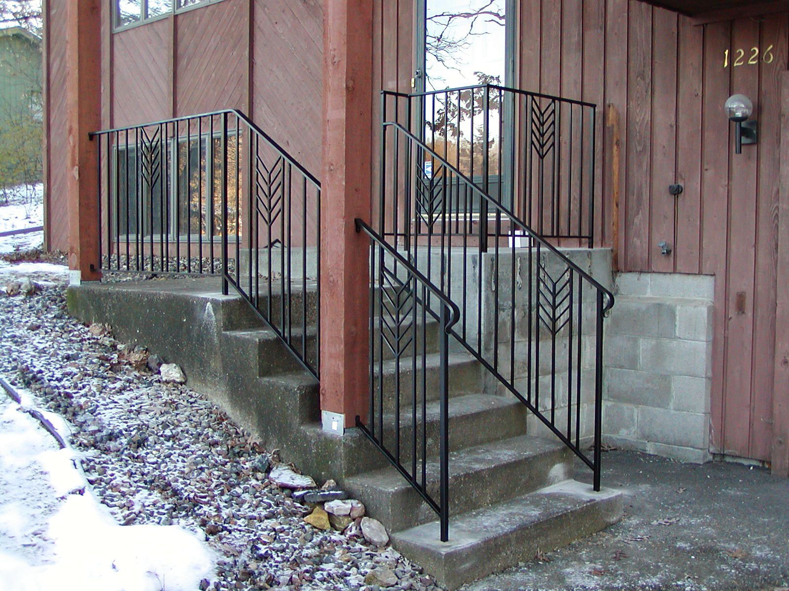 Black metal railings on concrete steps leading to a wooden building entrance.