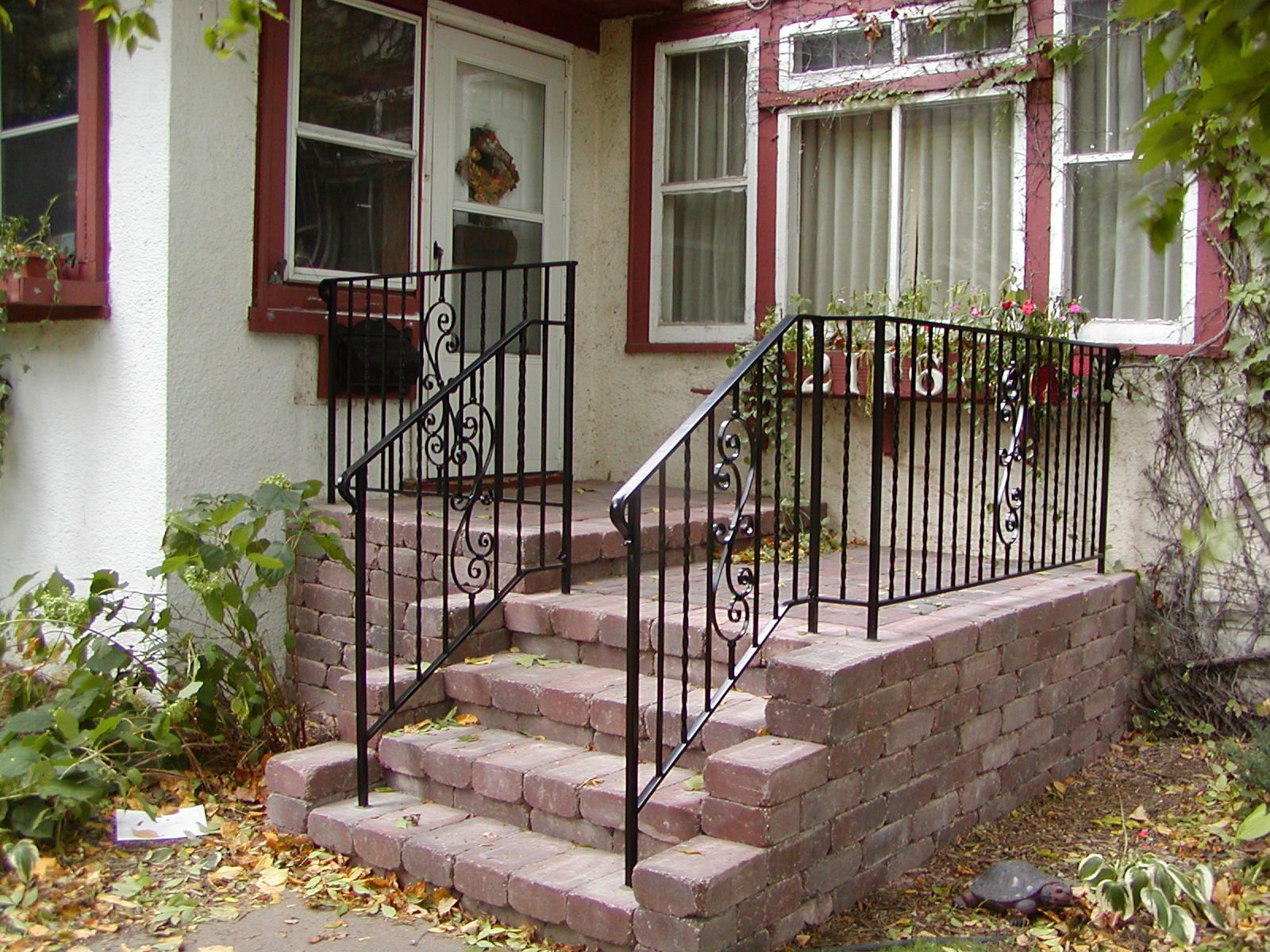Brick steps leading up to a house with black wrought-iron railings and a front door.