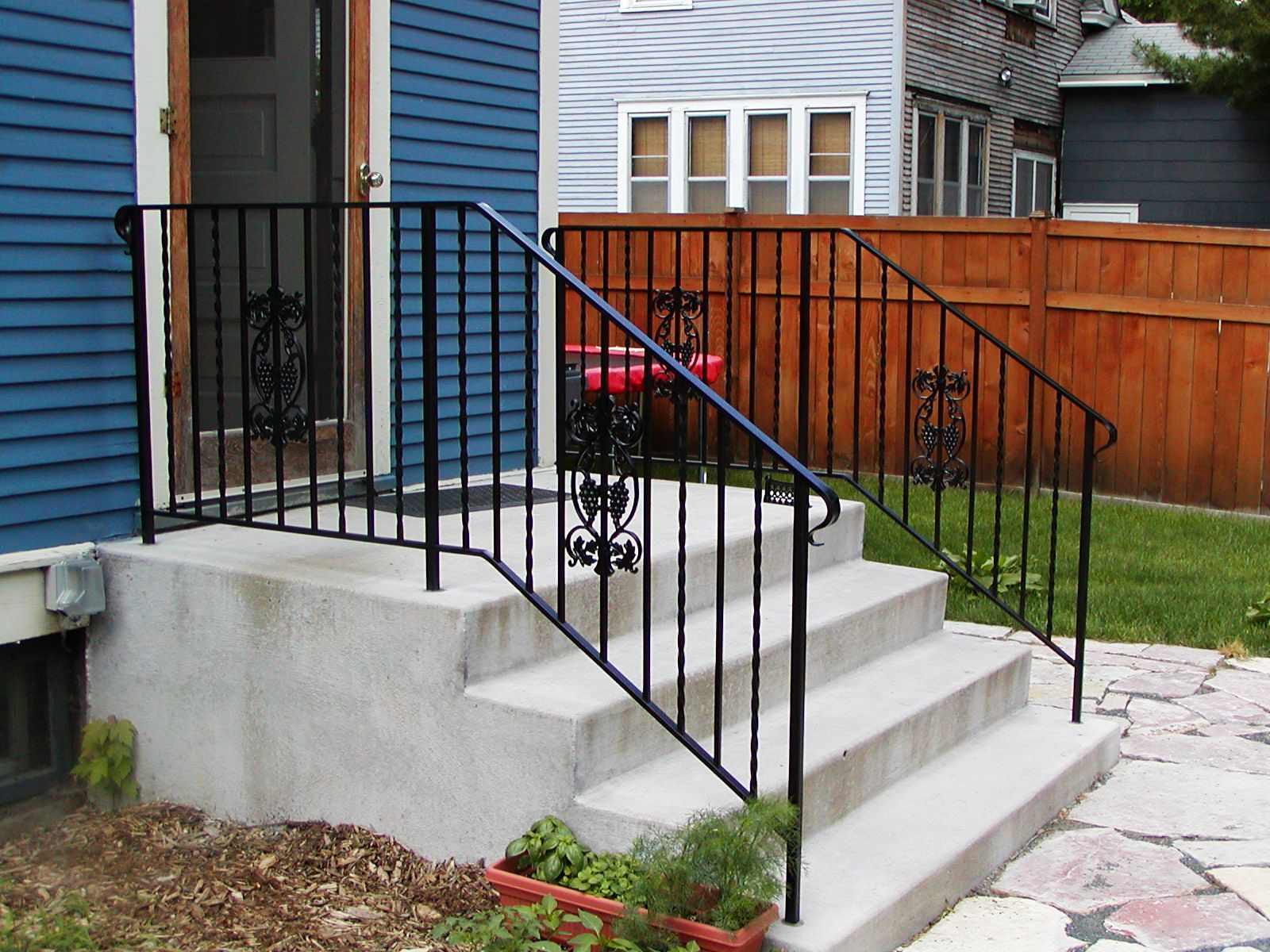 Black metal railing on concrete steps leading to a blue house entrance.