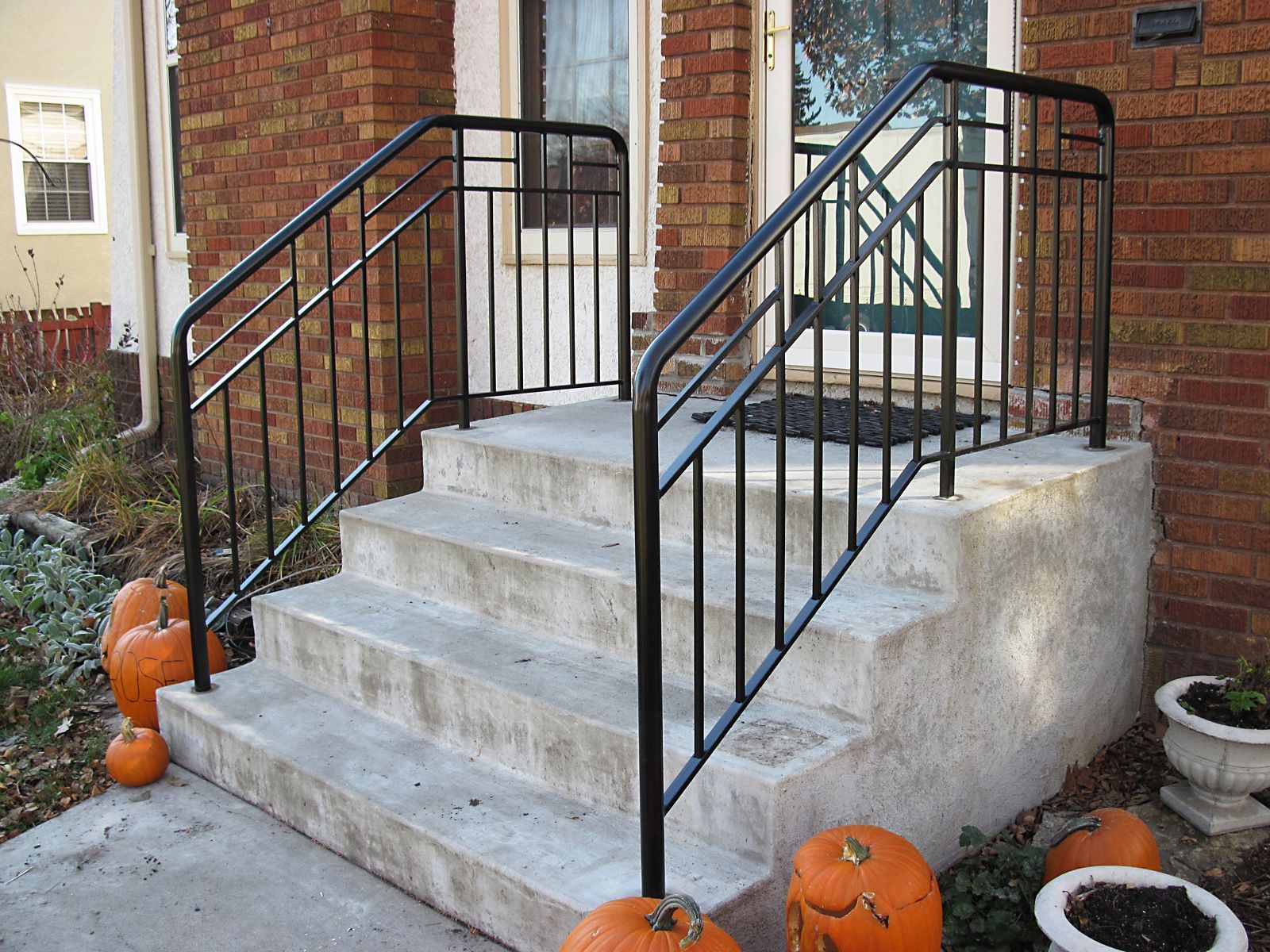 Exterior concrete steps with black metal railing, pumpkins, and a front door.