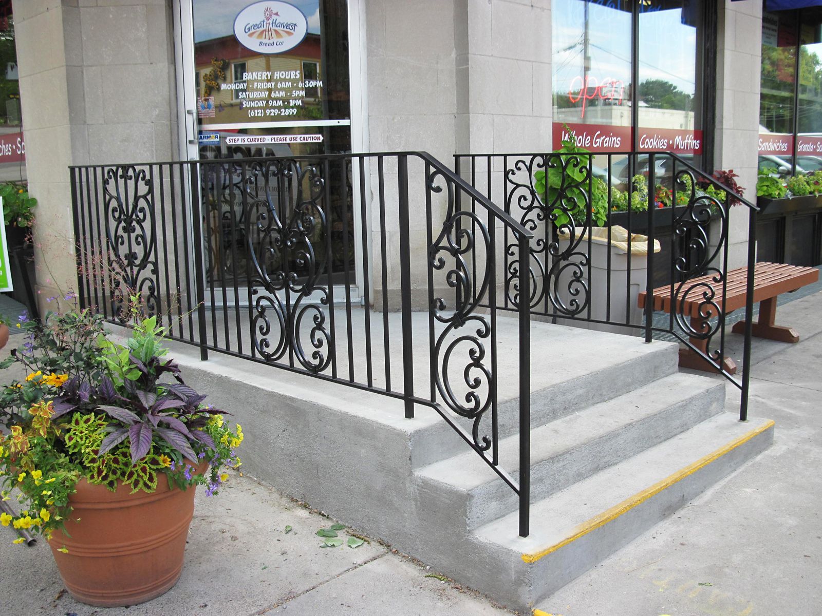 Entrance with concrete steps, black wrought iron railing, and potted plants.