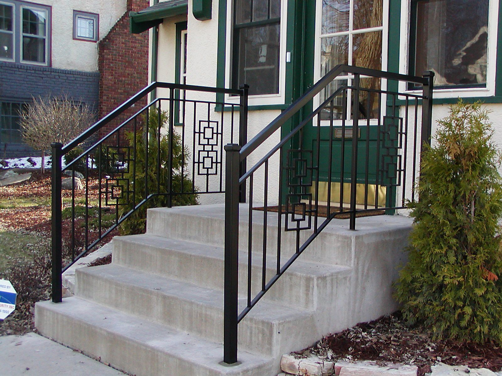 Black metal handrails on concrete steps leading to a house entrance.