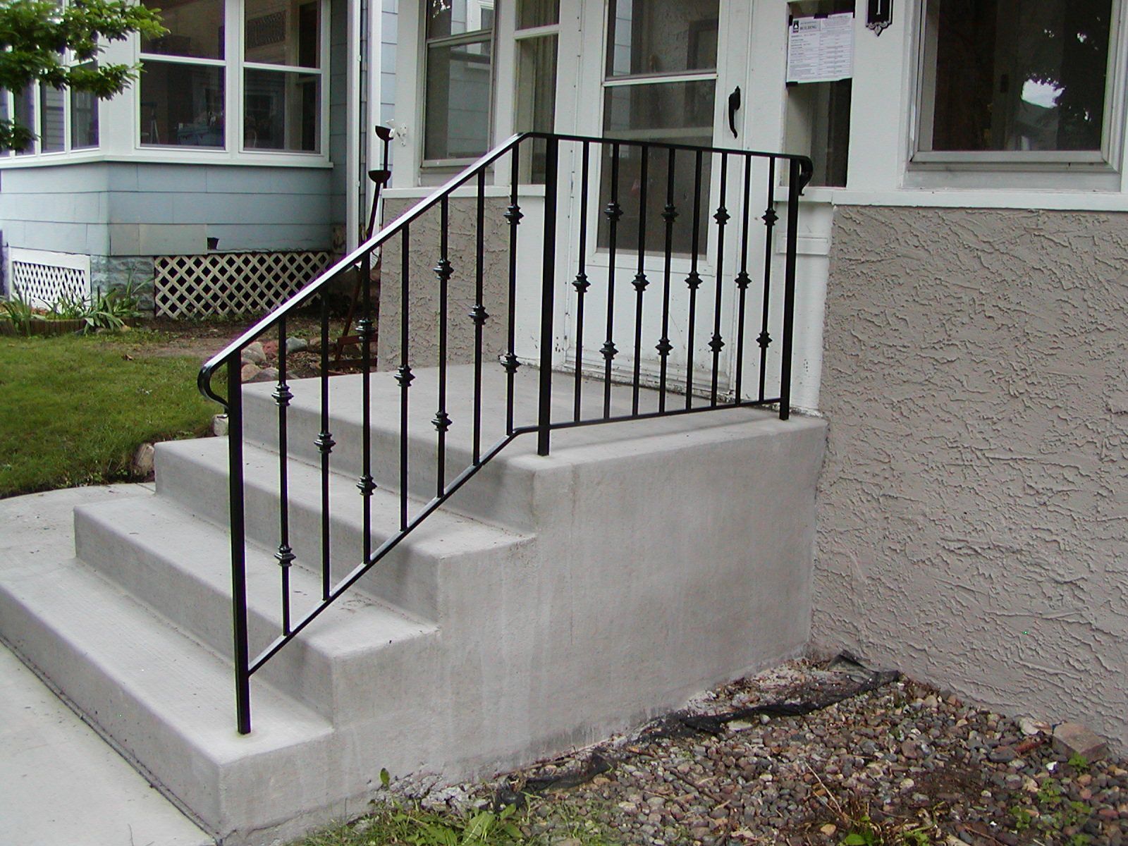 Concrete steps leading to a house with a black metal handrail.